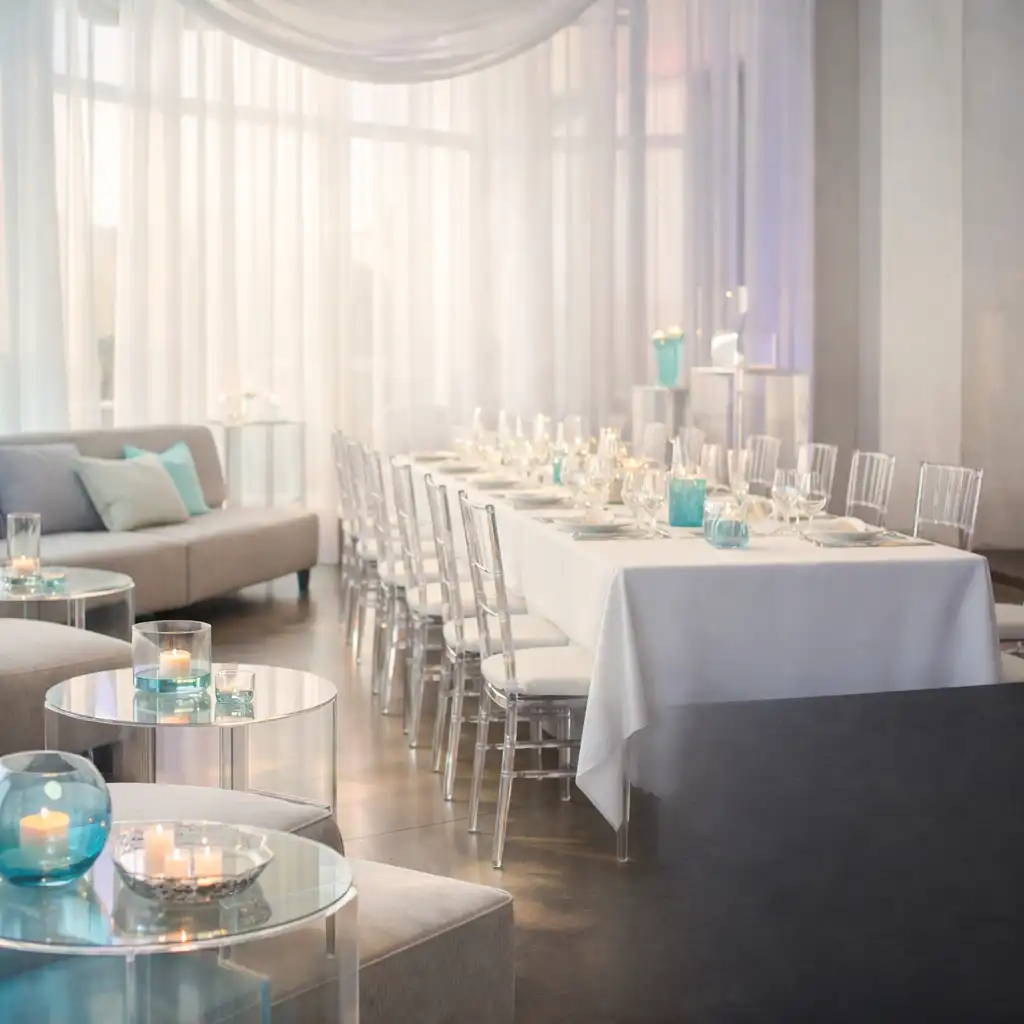 Lichtdurchflutete private Feier mit langem Tisch, Lounge-Elementen und dezenten Aqua-Lichtreflexen